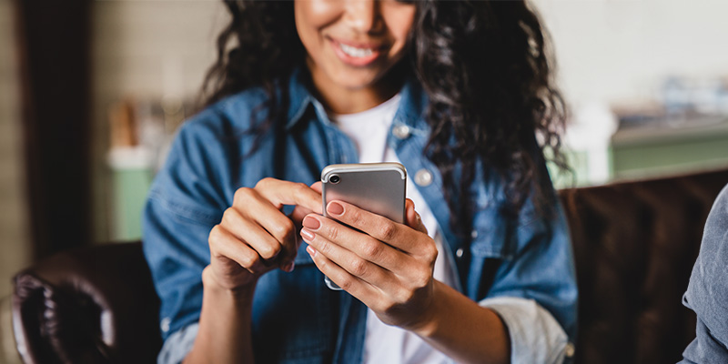 A person using a smartphone, with a blurred background featuring another individual.